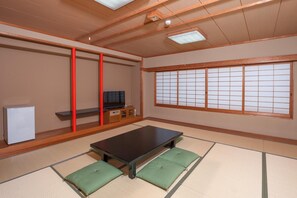 Una habitación tradicional japonesa con suelo de tatami, una mesa baja, un televisor y puertas correderas.