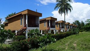 Filas de cabañas de madera con escaleras exteriores, rodeadas de exuberante follaje y una palmera.