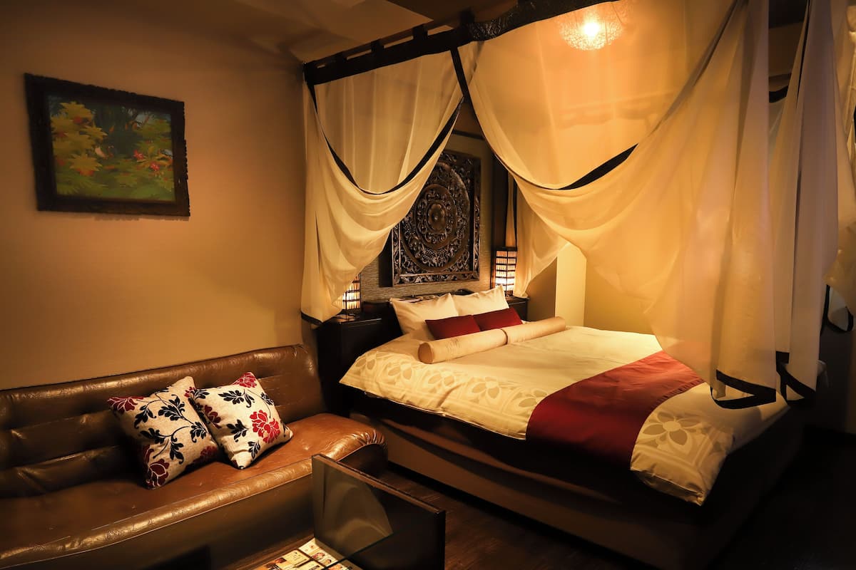 A room with a bed, a leather sofa, and a glass coffee table with magazines.
