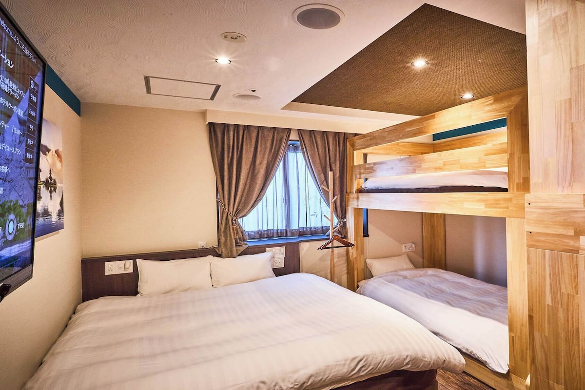 A room with bunk beds, a window with curtains, and a wall-mounted TV.