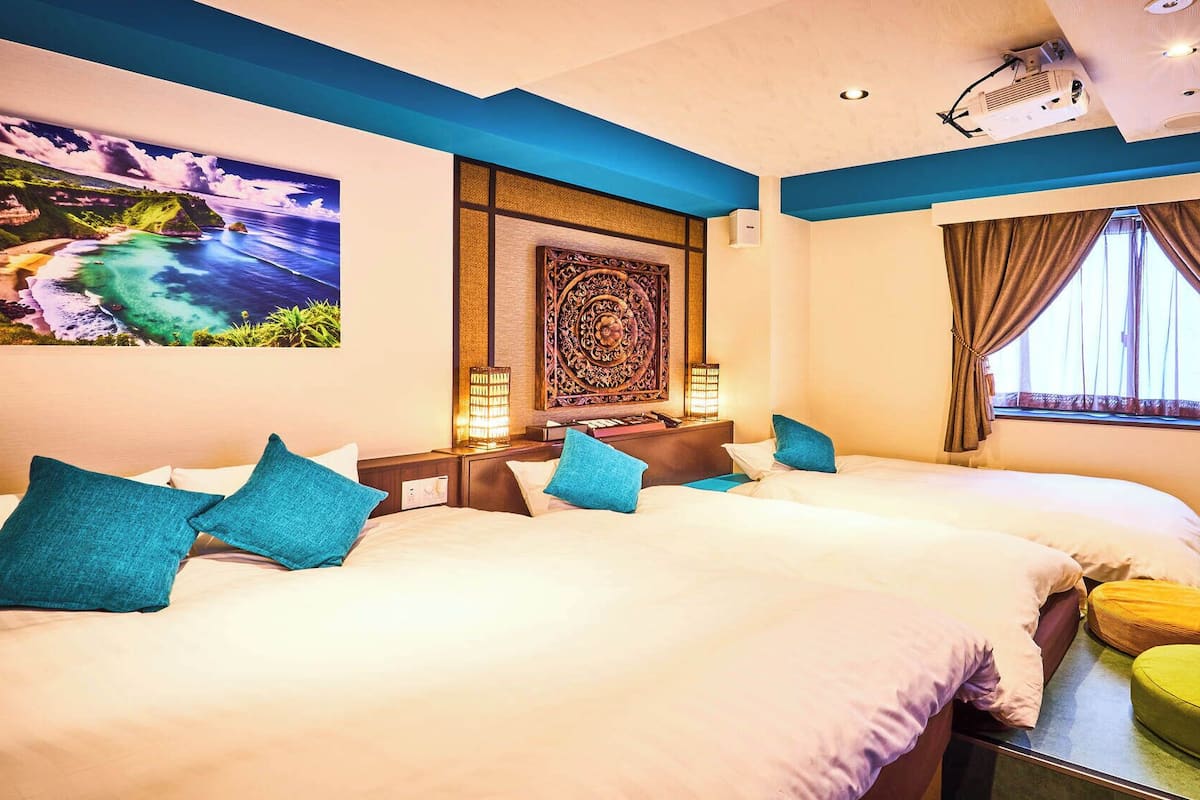 A hotel room with two beds, a desk, a lamp, and a view of the outdoors.
