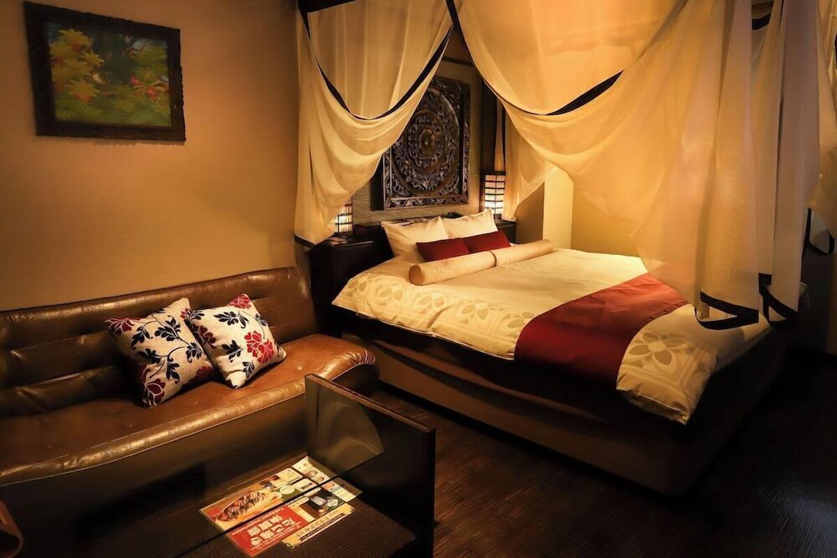 A room with a bed, a brown leather sofa, and a small table with a magazine.