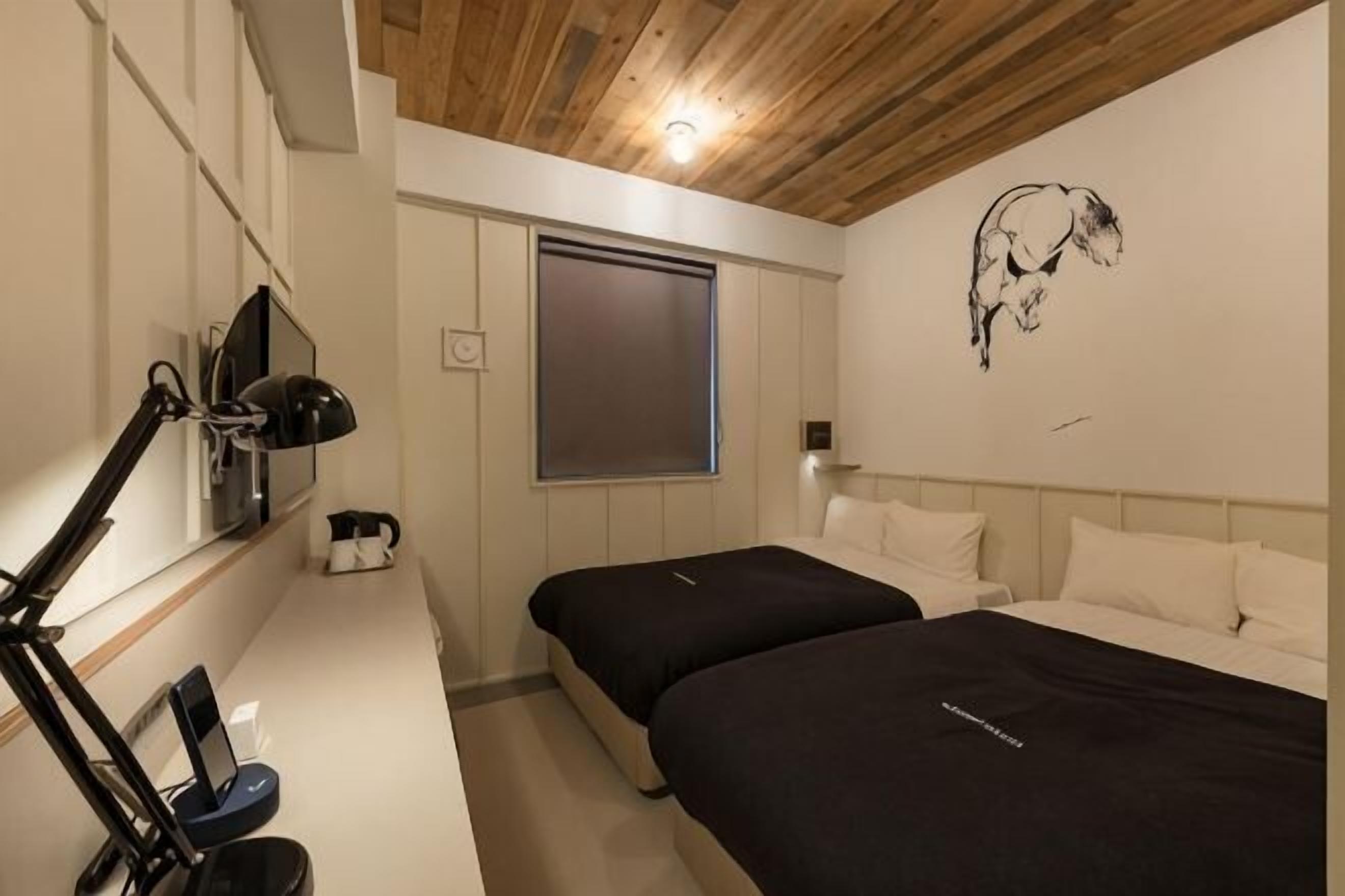 A bedroom with two beds, a desk with a computer, a TV, and a window.