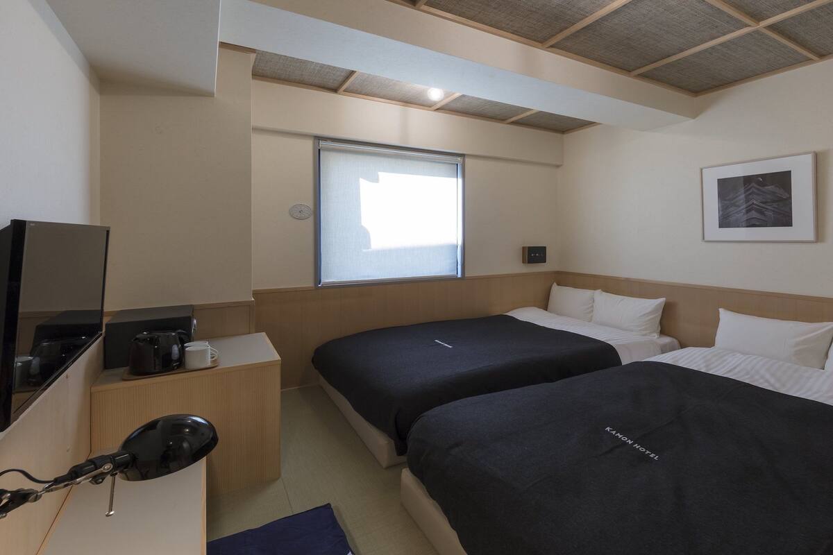 A hotel room with two beds, a TV, a coffee maker, and a window.
