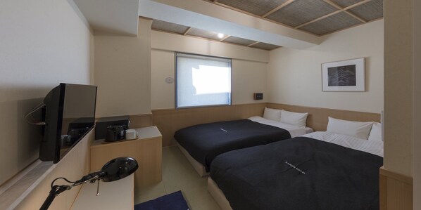 A hotel room with two beds, a TV, a coffee maker, and a window.