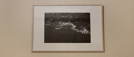 A framed black and white photograph of a coastal scene with a wooden pier and a boat.