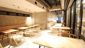 Een modern café interieur met houten tafels en stoelen, een bedieningsgedeelte en grote ramen.