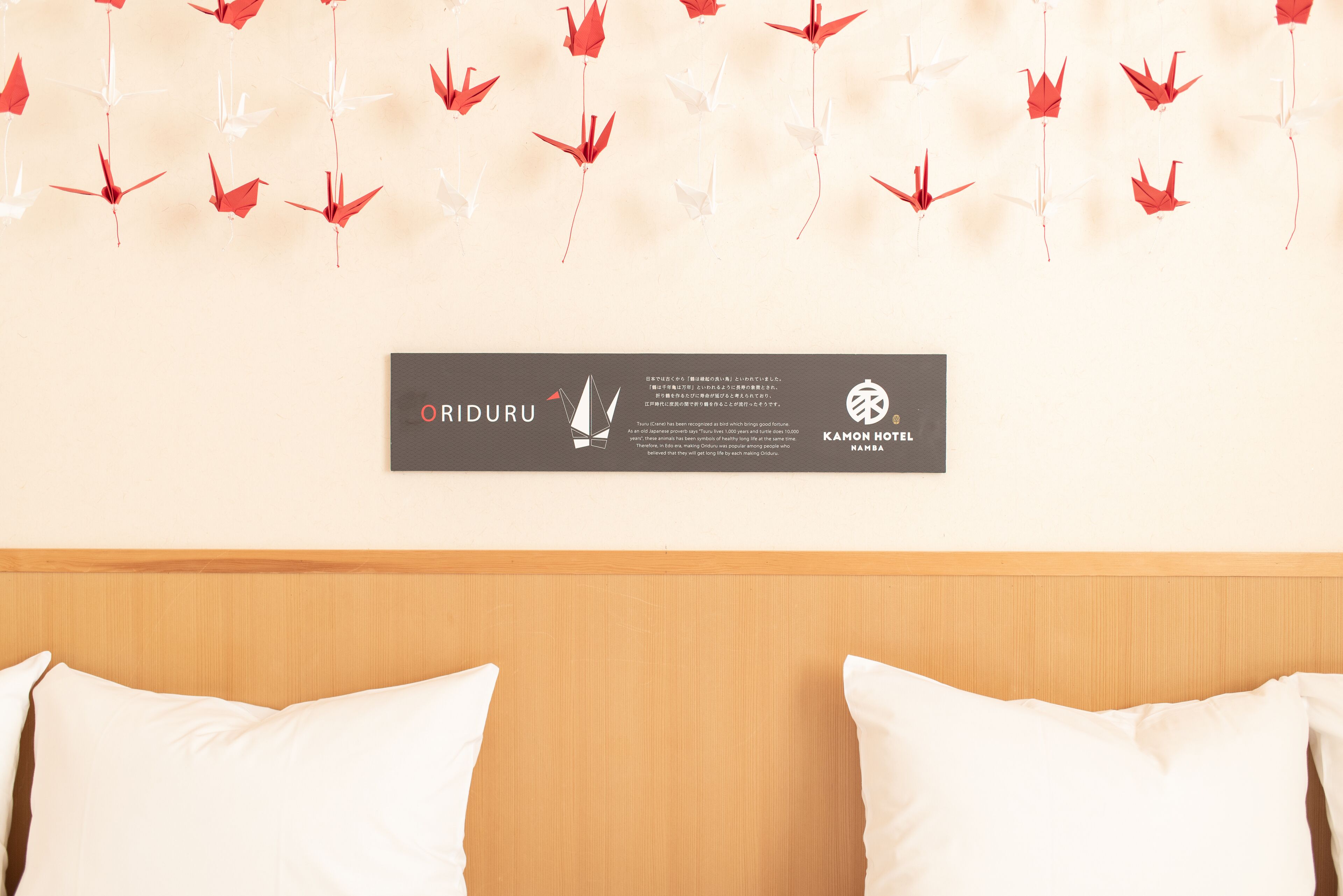 Een hotelkamer met een houten hoofdeinde, witte kussens en een wanddecoratie van origami kraanvogels.