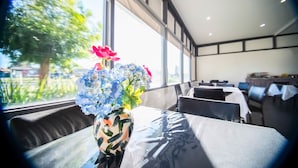 A dining area with tables and chairs, a vase with flowers, and a view of greenery outside. - Tamworth City Motel (South Tamworth)