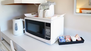 Een witte magnetronoven met digitaal display en bedieningspaneel, een witte waterkoker, en een dienblad met koffiepakketjes op een witte aanrechtplaat.