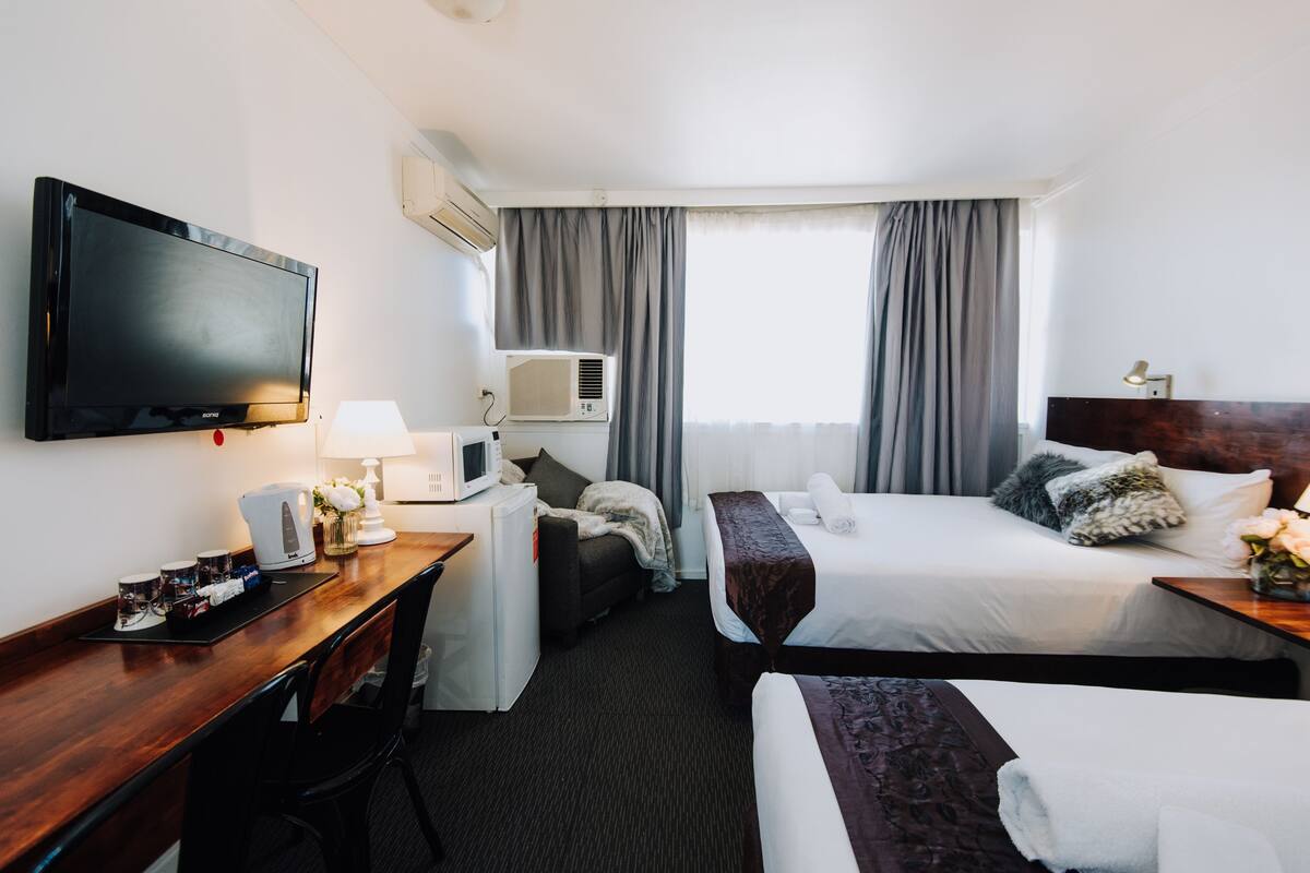 Une chambre d’hôtel avec deux lits, un bureau doté d’un téléviseur à écran plat, un four à micro-ondes, une lampe et une fenêtre avec des rideaux.