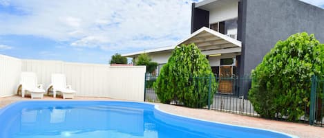 Una piscina al aire libre, sillones reclinables de piscina