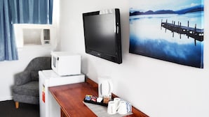 Hotelkamer met een flatscreen televisie, een magnetron, een koffiezetapparaat en een ontbijtbakje met koffiekopjes en gebak.