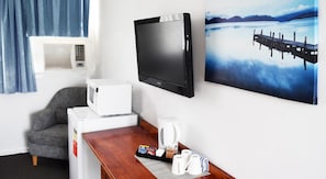 Une chambre d’hôtel équipée d’une télévision à écran plat, d’un four à micro-ondes, d’une machine à café et d’un plateau de petit-déjeuner comprenant des tasses à café et des viennoiseries.