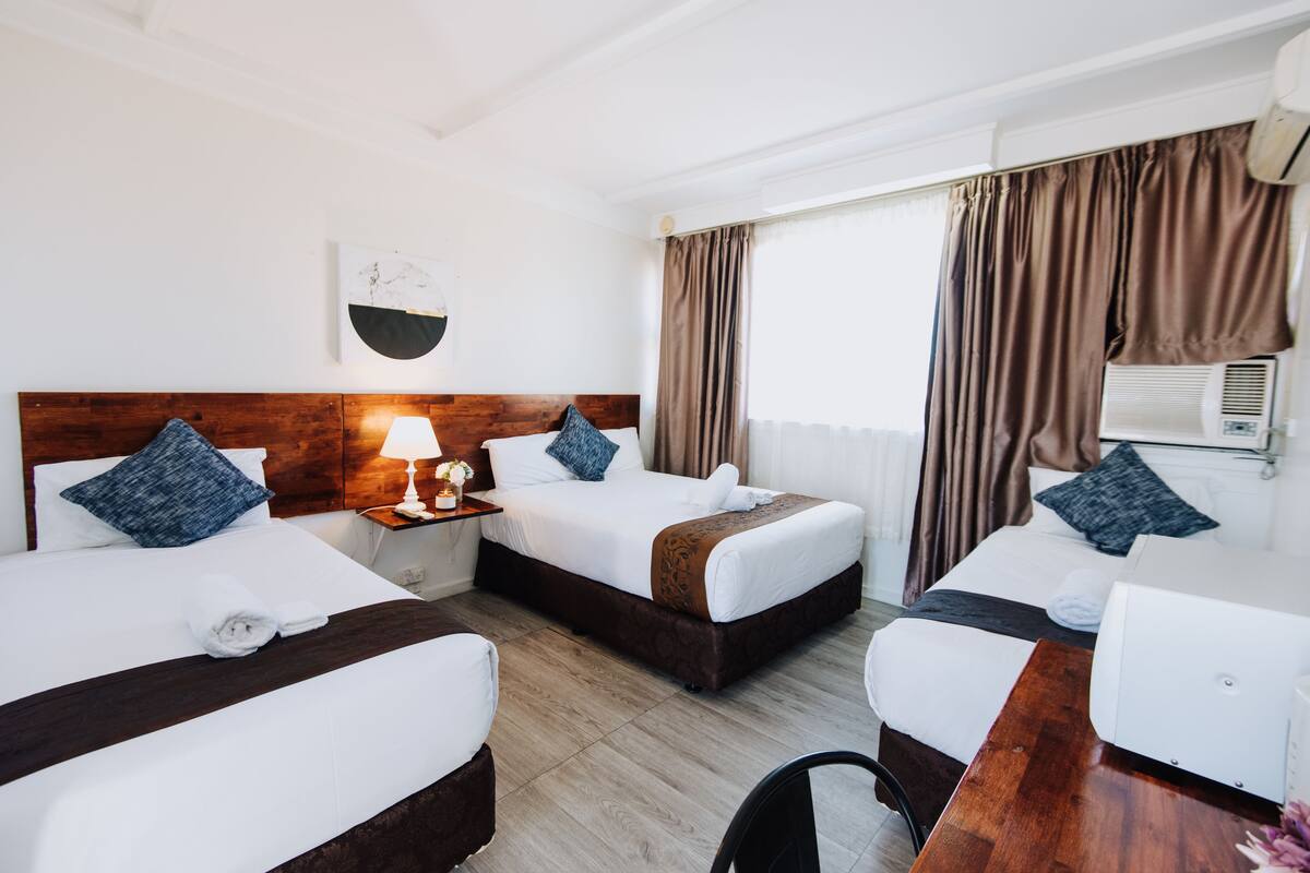Une chambre d’hôtel avec deux lits, un bureau, une lampe et un appareil de climatisation.
