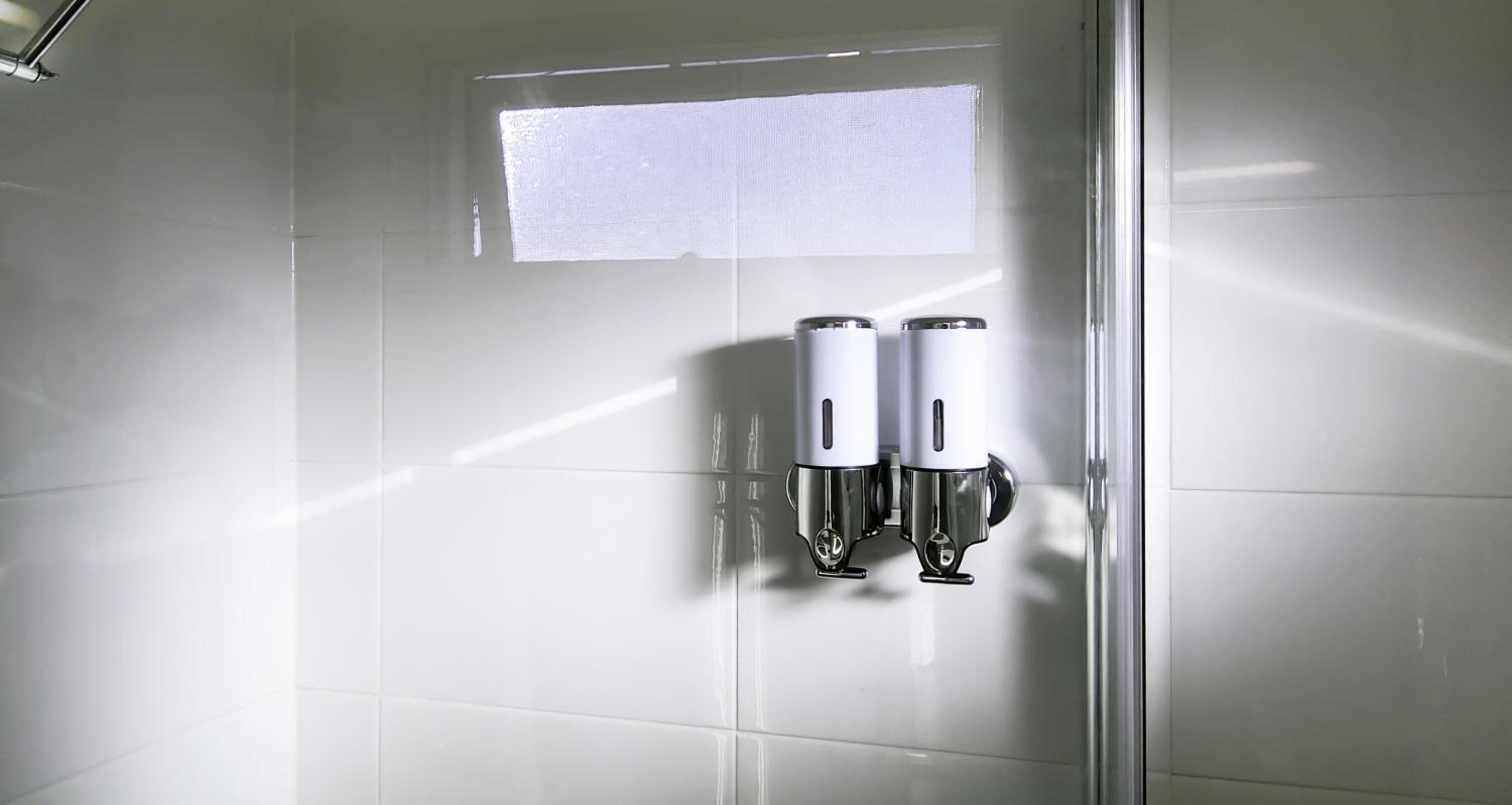 Un baño con dispensador de gel hidroalcohólico fijado a la pared.