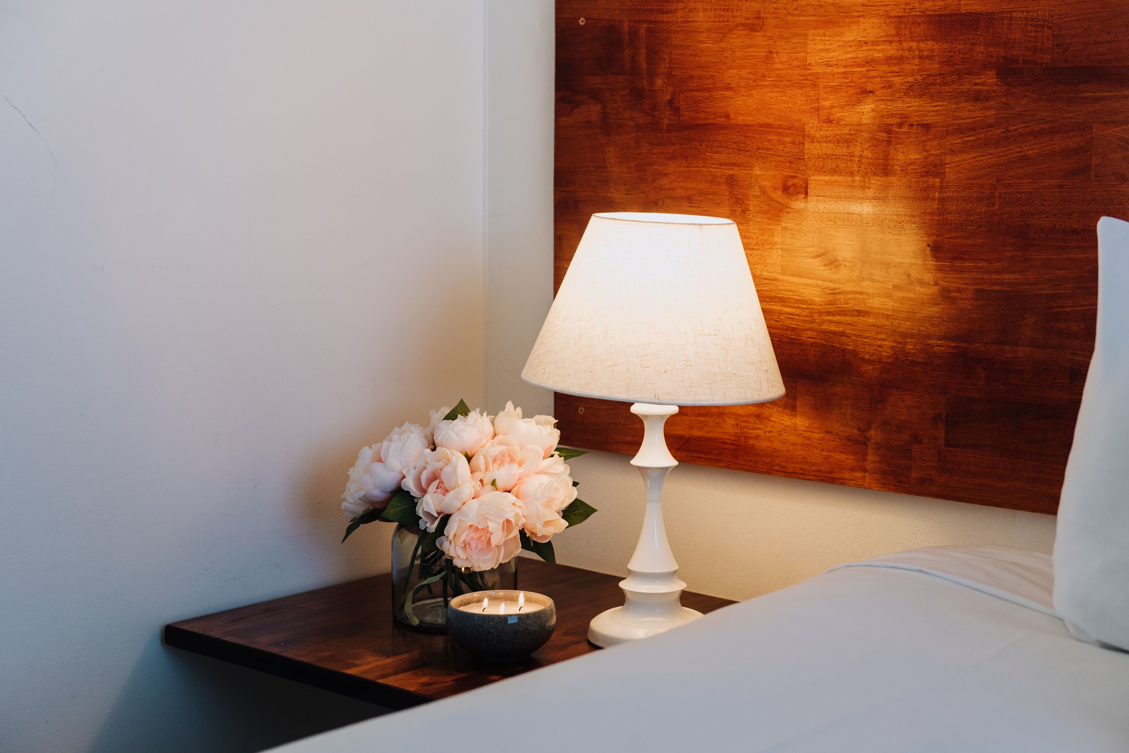 A neatly arranged bedside table with a white lamp, a vase of flowers, and a candle.
