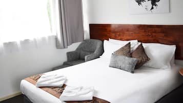 Una habitación de hotel con una cama grande, un sillón gris y un cabecero de madera.