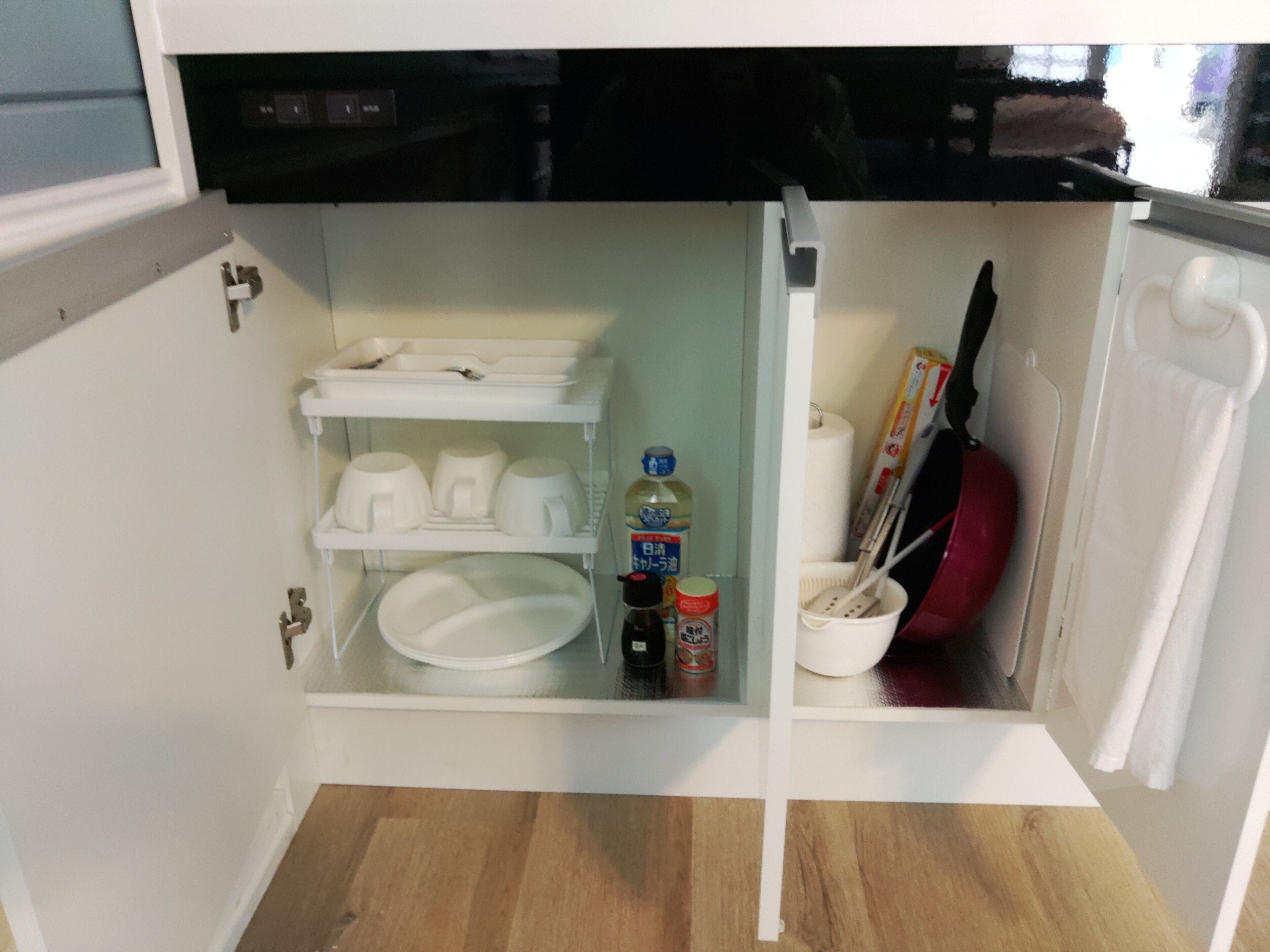 A compact kitchen with white cabinets, a dishwasher, and a small countertop area with a dish rack, a bottle, and a red-handled kitchen tool.