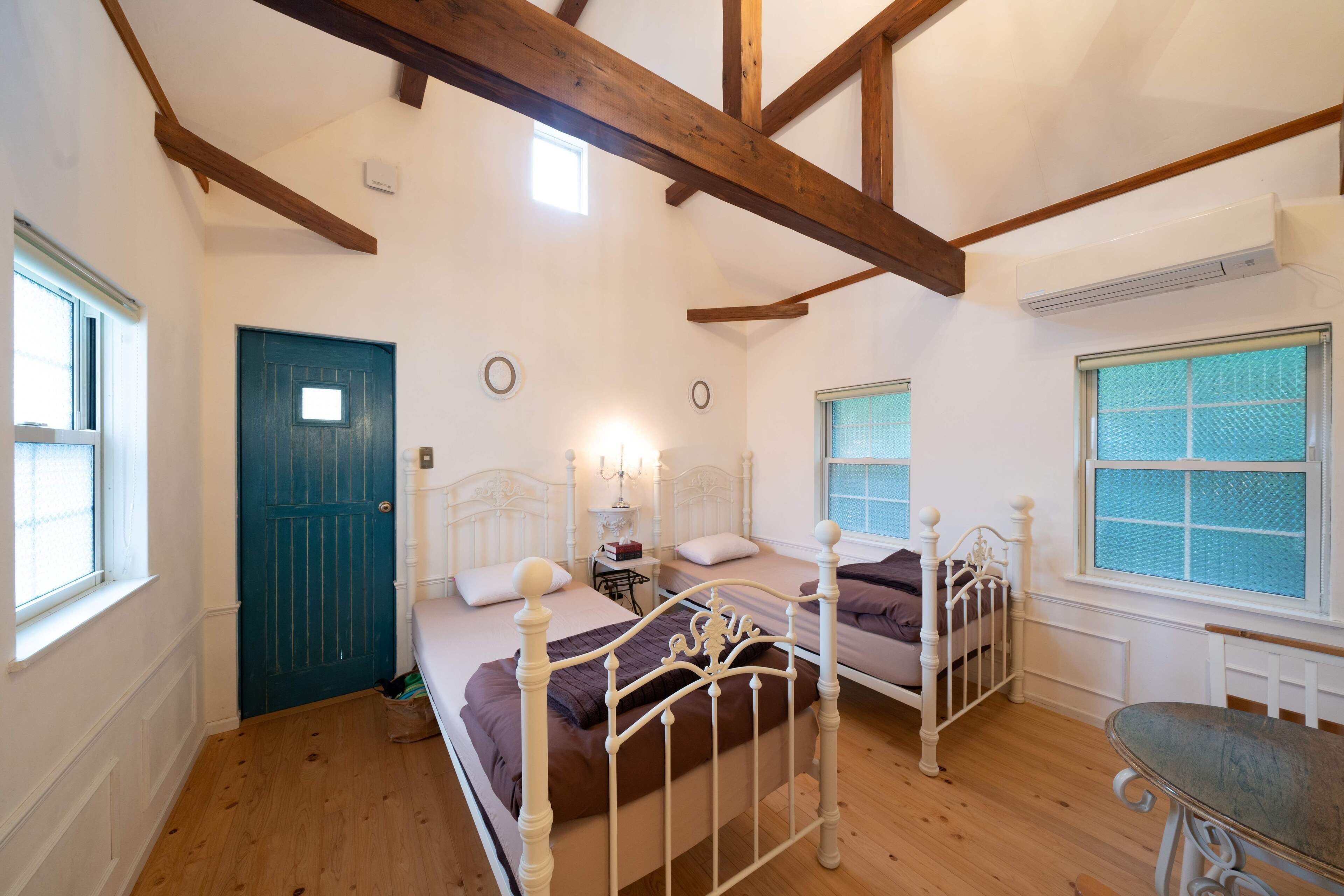 Ein Schlafzimmer mit zwei Betten, Holzboden, einer blauen Tür und einem Fenster mit Blick.