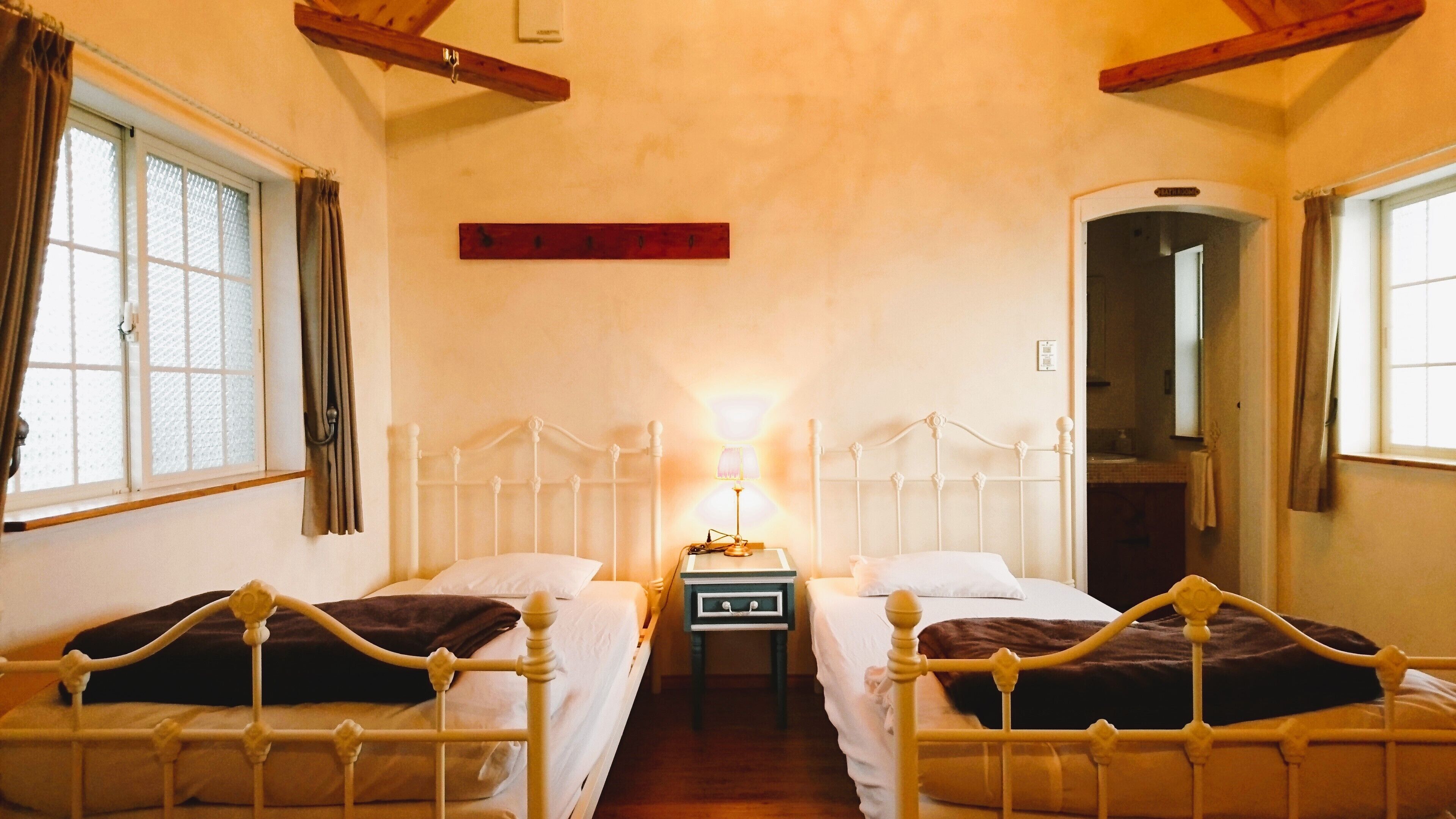 A room with two beds, a nightstand with a lamp, and a wooden ceiling beam.