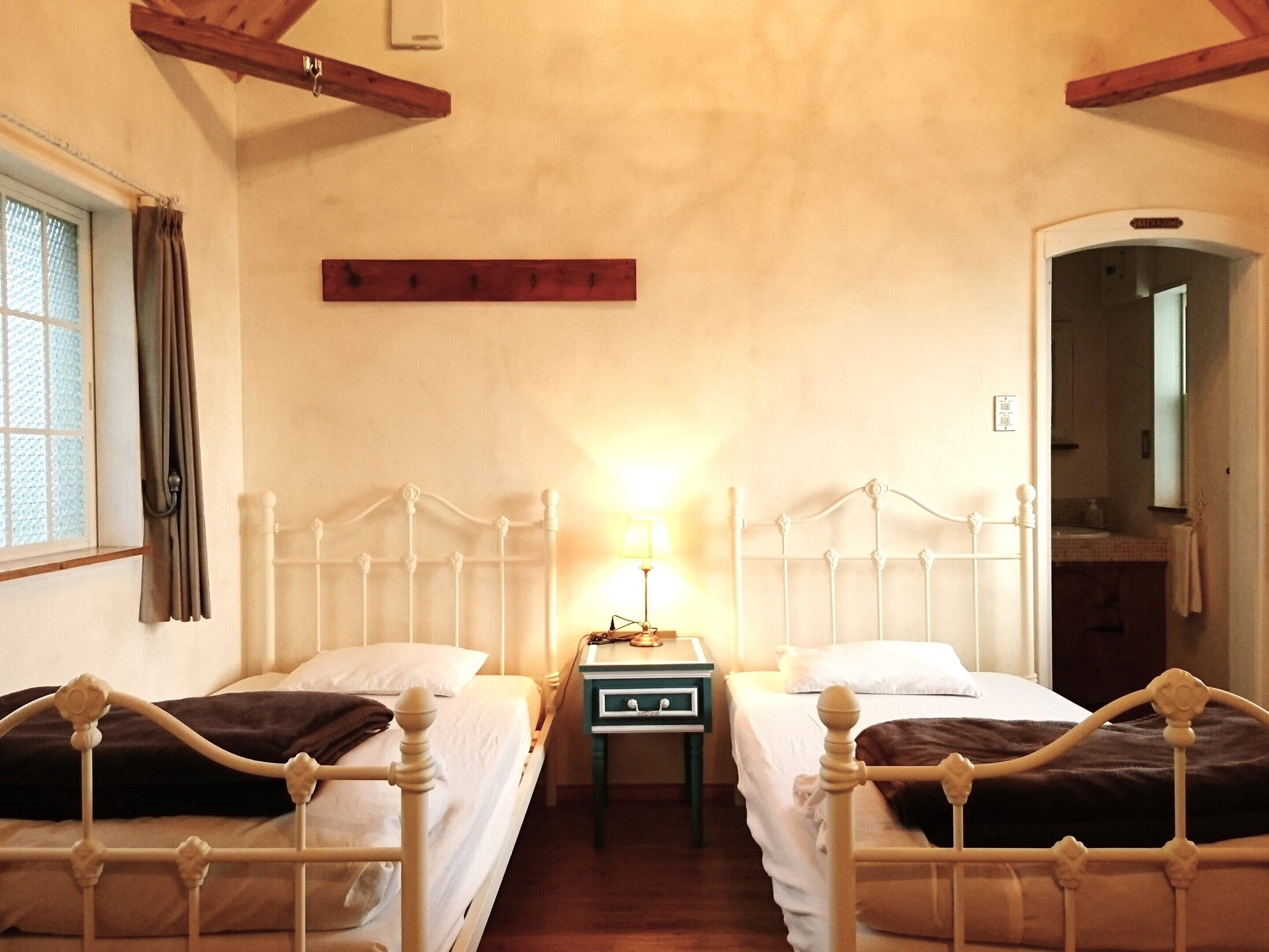 A room with two beds, a nightstand, a lamp, and a window with curtains.