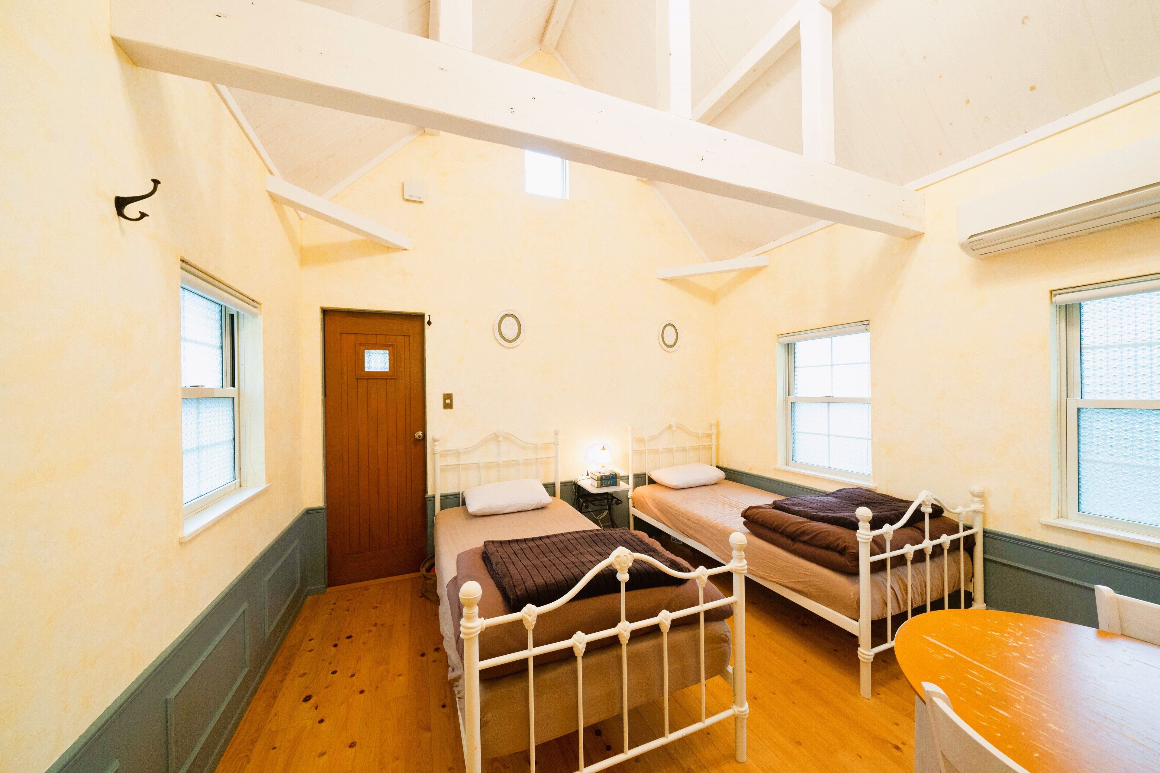 A room with two beds, a wooden floor, a table, and a window.