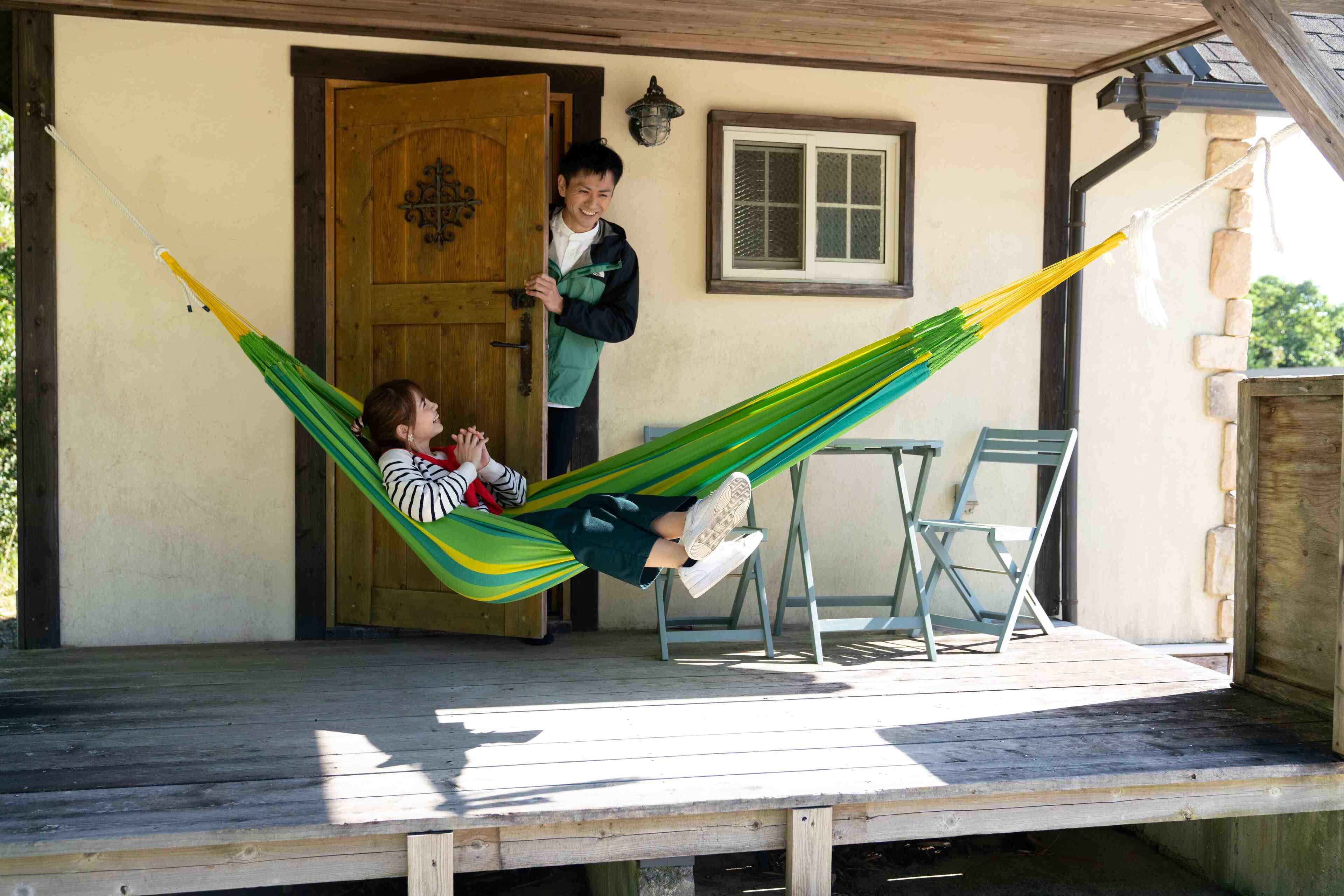 A wooden porch with a hammock, a wooden door, and a window.