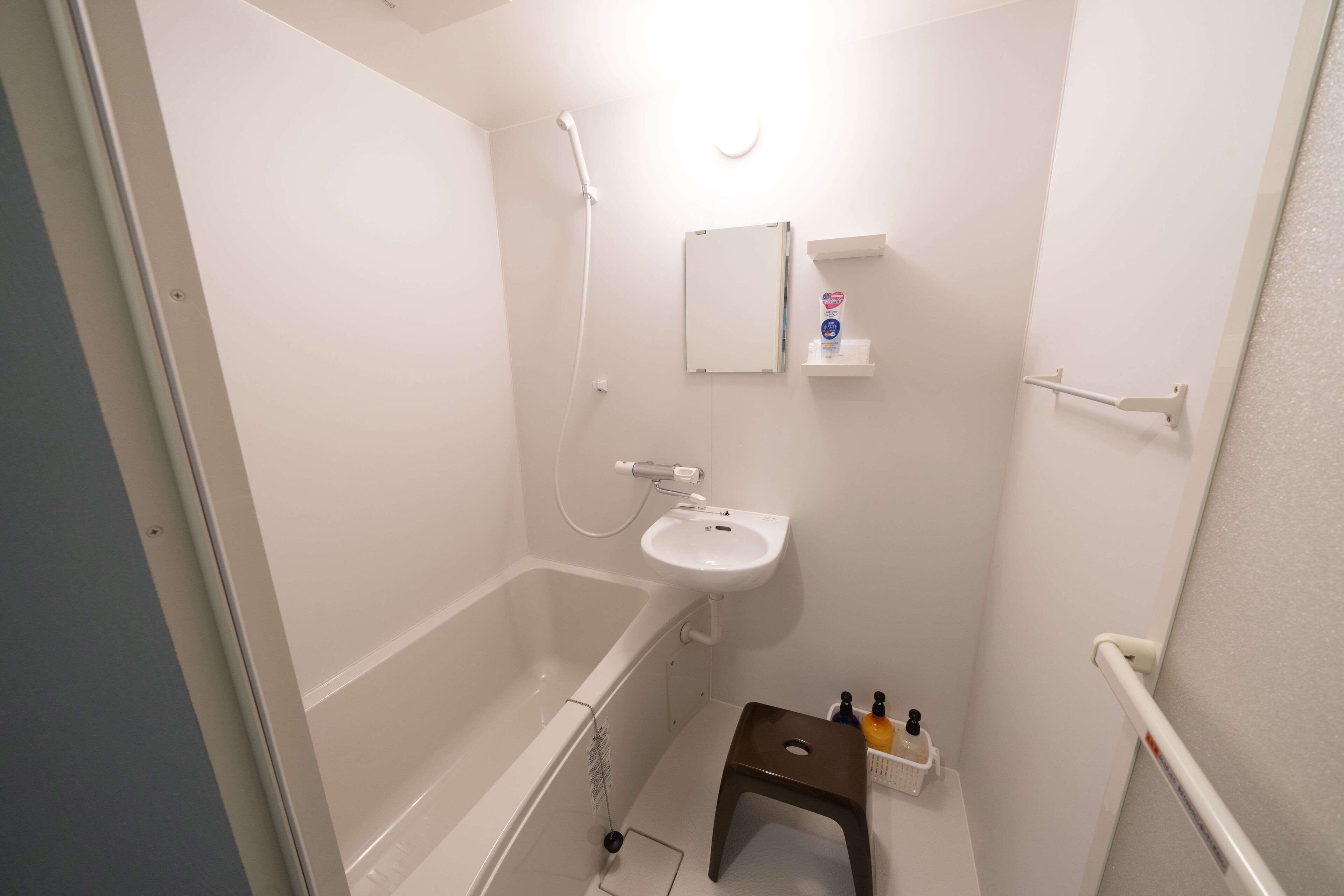 Un baño pequeño y blanco con una bañera, un lavabo y un taburete pequeño.