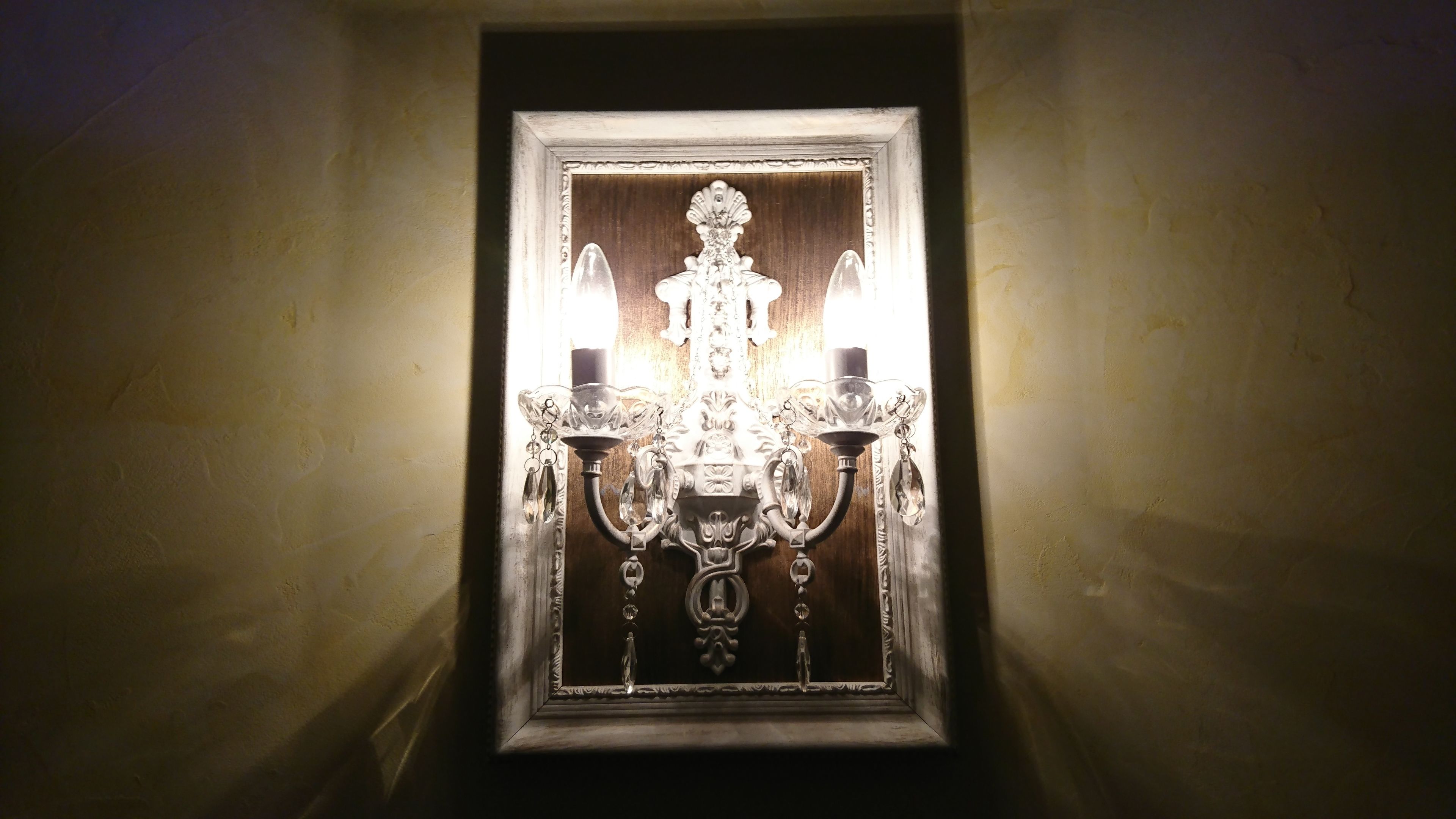 Eine wandmontierte Chandelieber mit mehreren, kerzenartigen Lichtern und Kristallverzierungen.