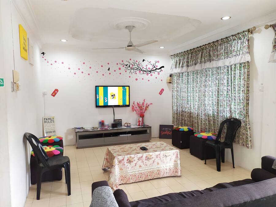 Una sala de estar con un televisor de pantalla plana, ventilador de techo, una mesita con motivos florales y un sofá.