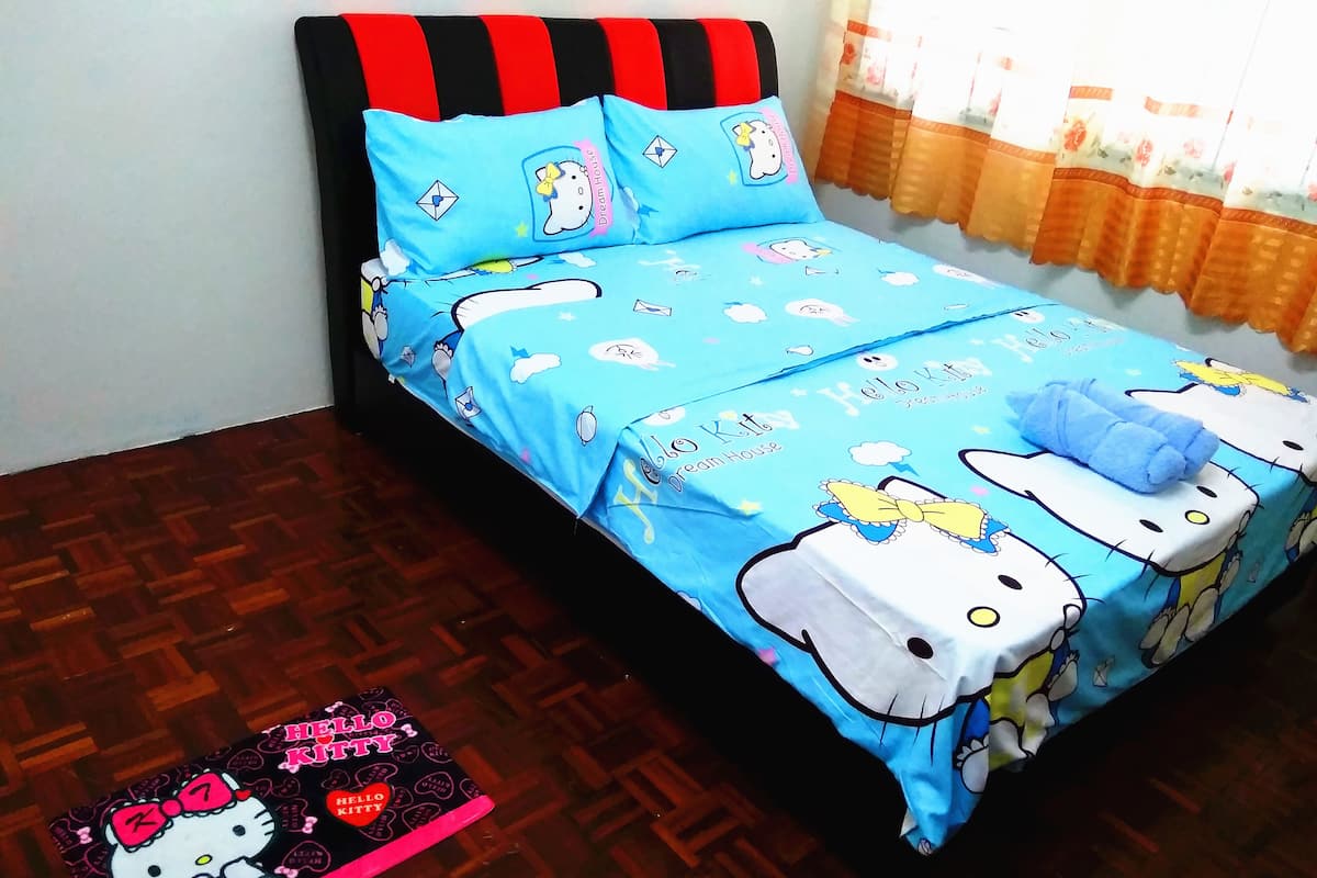 A bed with a Hello Kitty themed bedspread and pillows, a Hello Kitty mat on the floor, and a window with curtains.