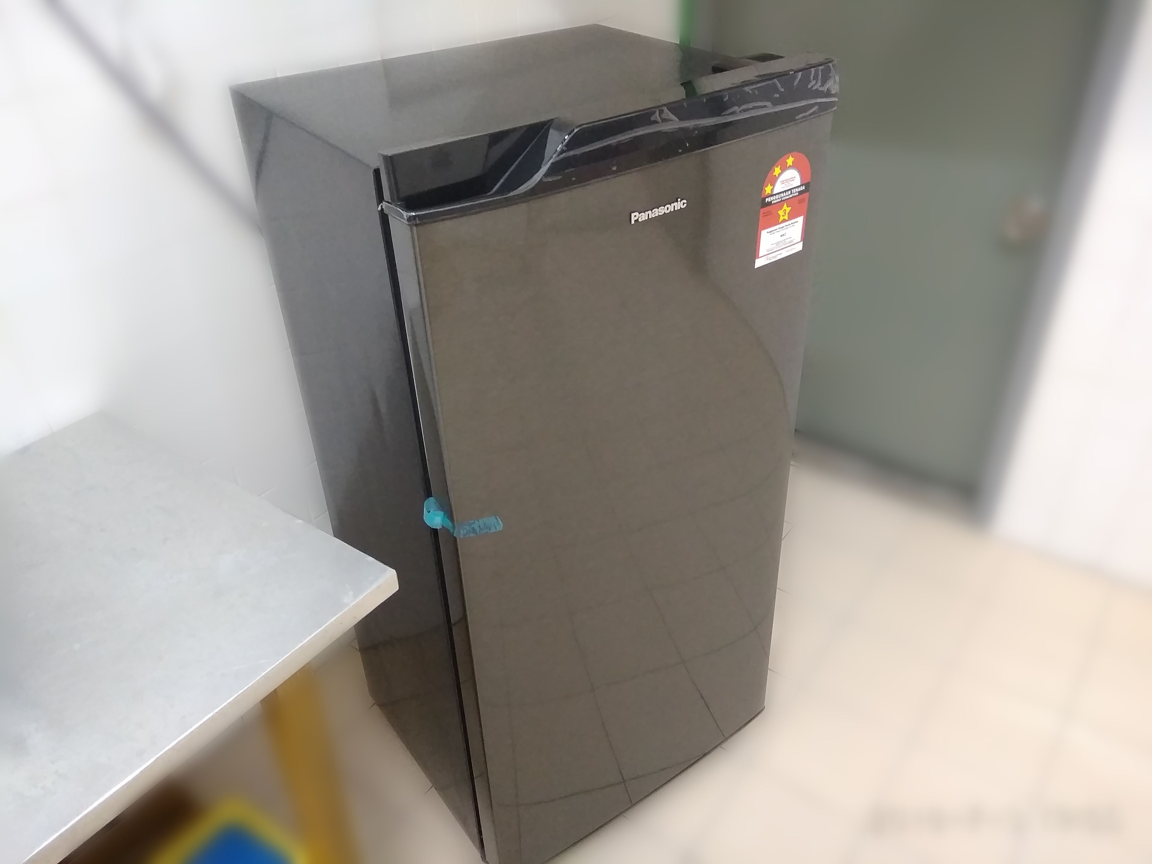 Un refrigerador compacto y de color oscuro con una etiqueta de marca visible y un adhesivo en la puerta.