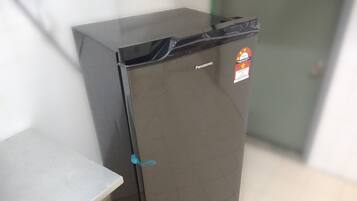 Un refrigerador compacto y de color oscuro con una etiqueta de marca visible y un adhesivo en la puerta.