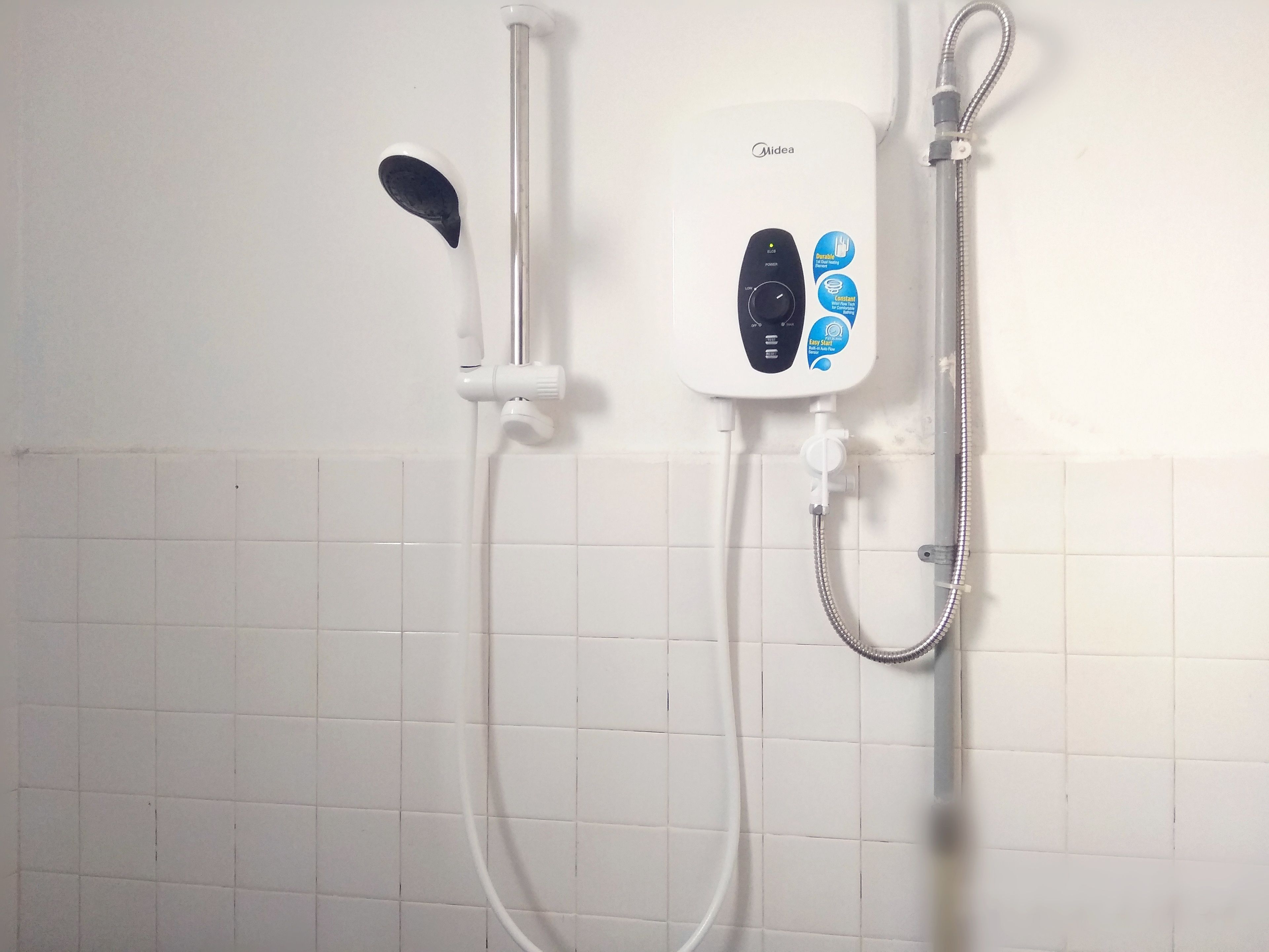 A wall-mounted shower unit with a control panel, a handheld showerhead, and a flexible hose.