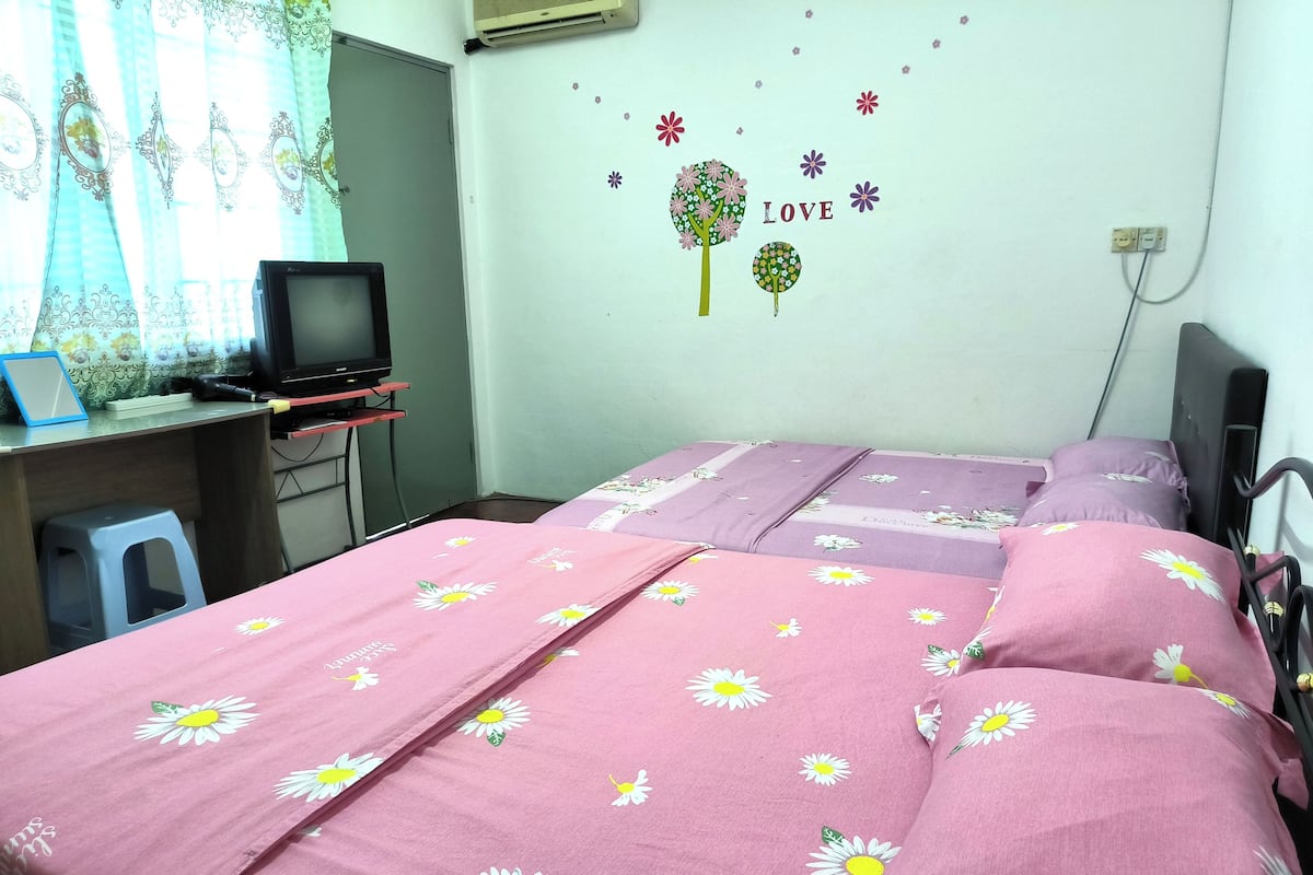 A bedroom with two beds, a desk with a computer, and a wall decoration.