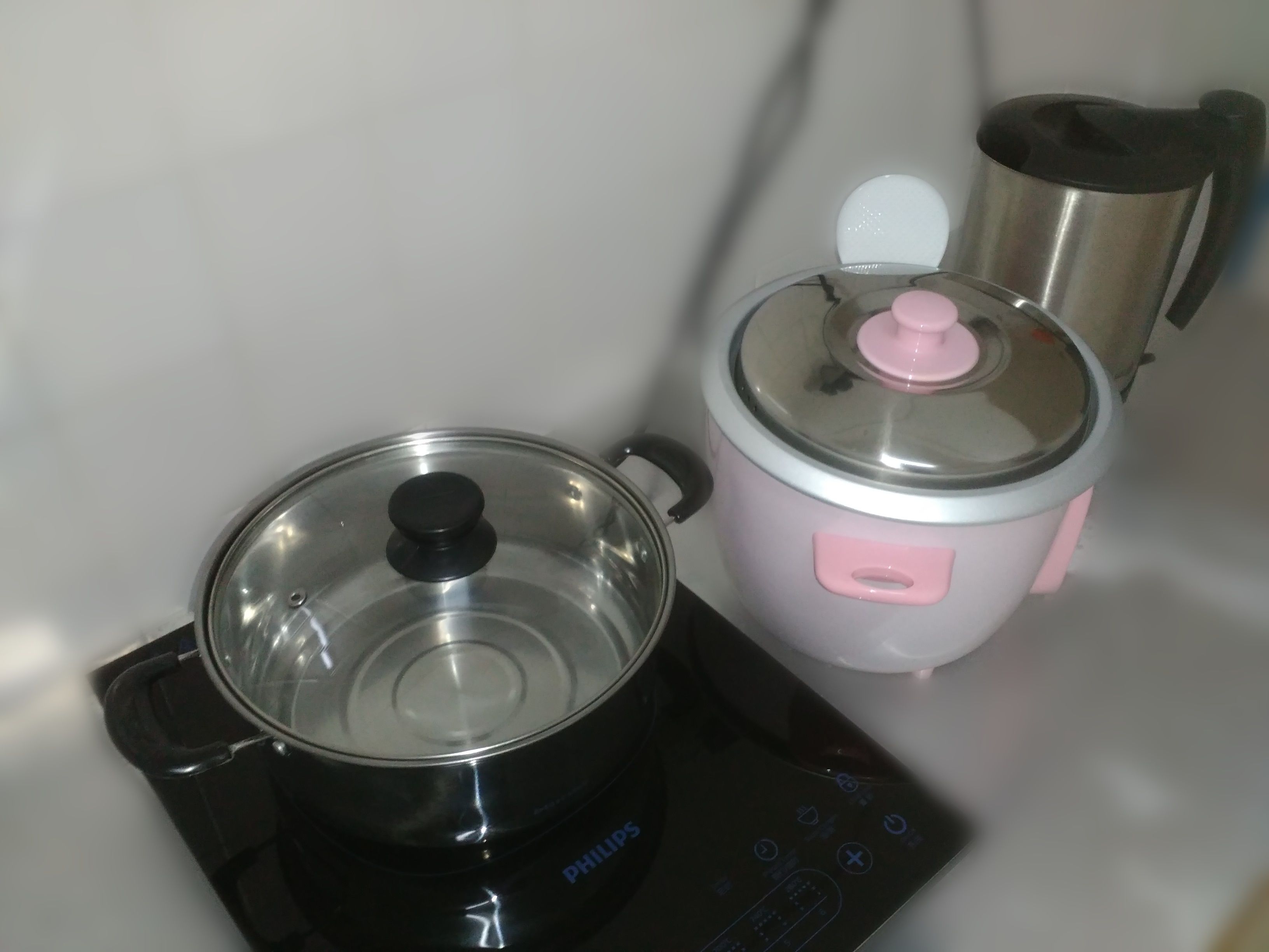A kitchen with a black induction cooktop and a pink slow cooker.