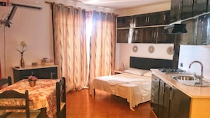 A compact kitchen with a dining area, a bed, and a small table with a vase. - Porto Antigo (Sal)