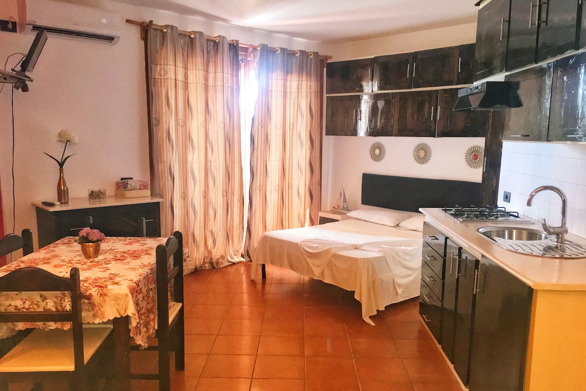 A compact kitchen with a dining area, a bed, and a small table with a vase.