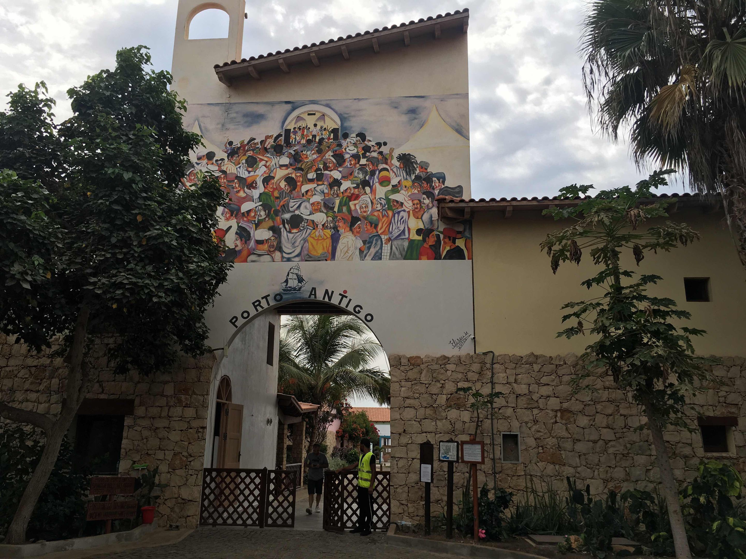Un bâtiment orné d’une fresque représentant une foule, avec l’inscription « Porto Antigo » au-dessus d’une arche.