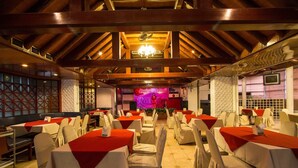 A banquet hall with tables set for events, featuring a stage with a pink backdrop and a chandelier.