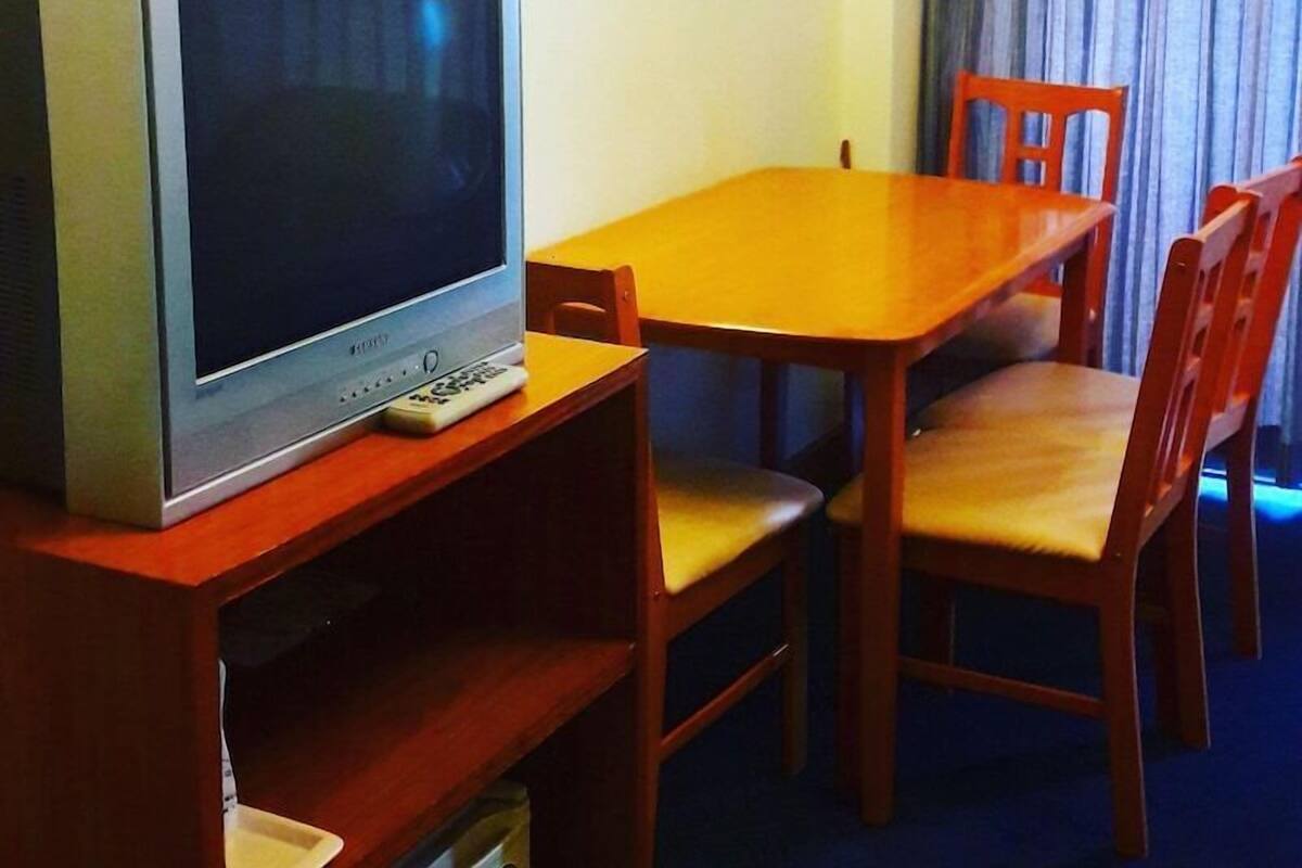 Une pièce comprenant un téléviseur posé sur un meuble en bois, une table en bois et quatre chaises.