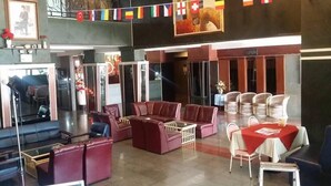 A lobby with leather sofas, wicker chairs, and a dining area with a red tablecloth.