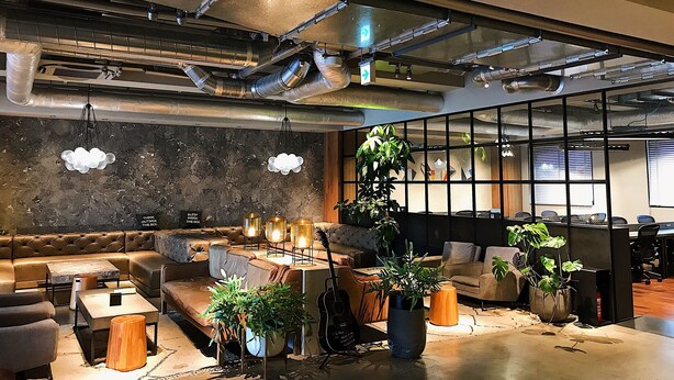 Een moderne kantoorruimte met een leren bank, een houten bijzettafeltje en potplanten.