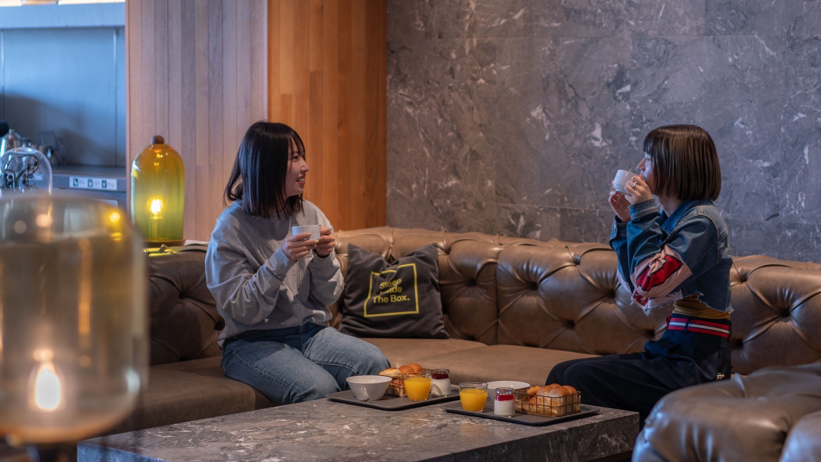 Two people sitting on a leather couch with a tray of breakfast items in front of them.