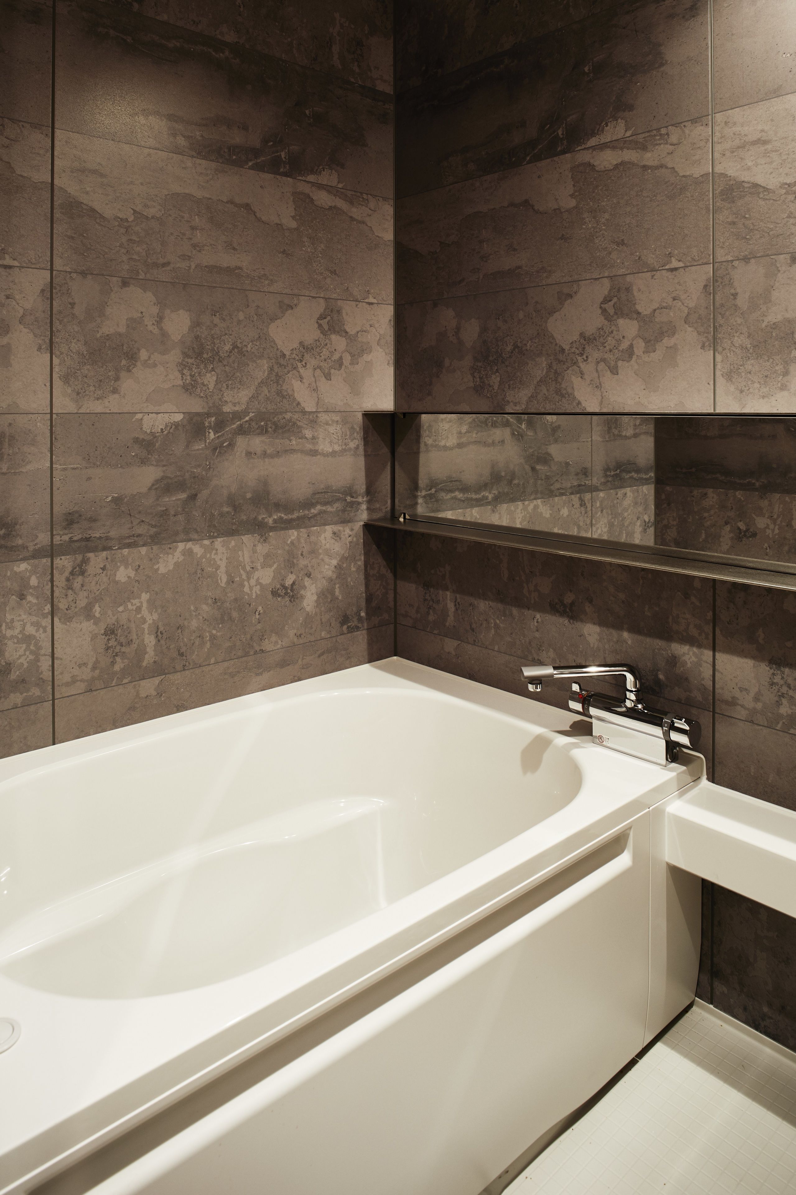 Une salle de bain moderne avec une baignoire sur pieds, des murs recouverts de carreaux foncés et un design minimaliste.