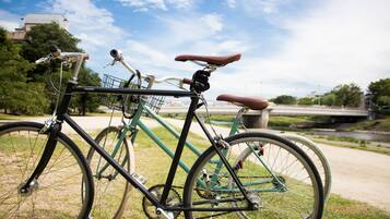 A bicycle with a basket and a seat, parked on grass with a bridge and trees in the background.