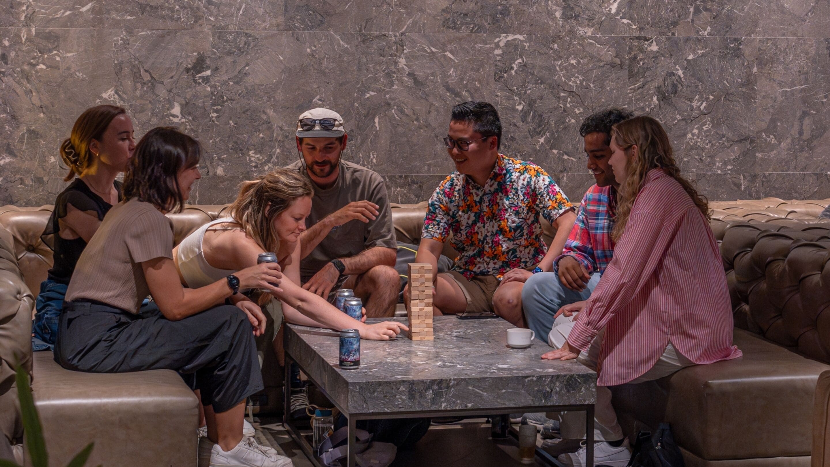 A group of people playing a board game on a marble table in a lounge area with leather couches.