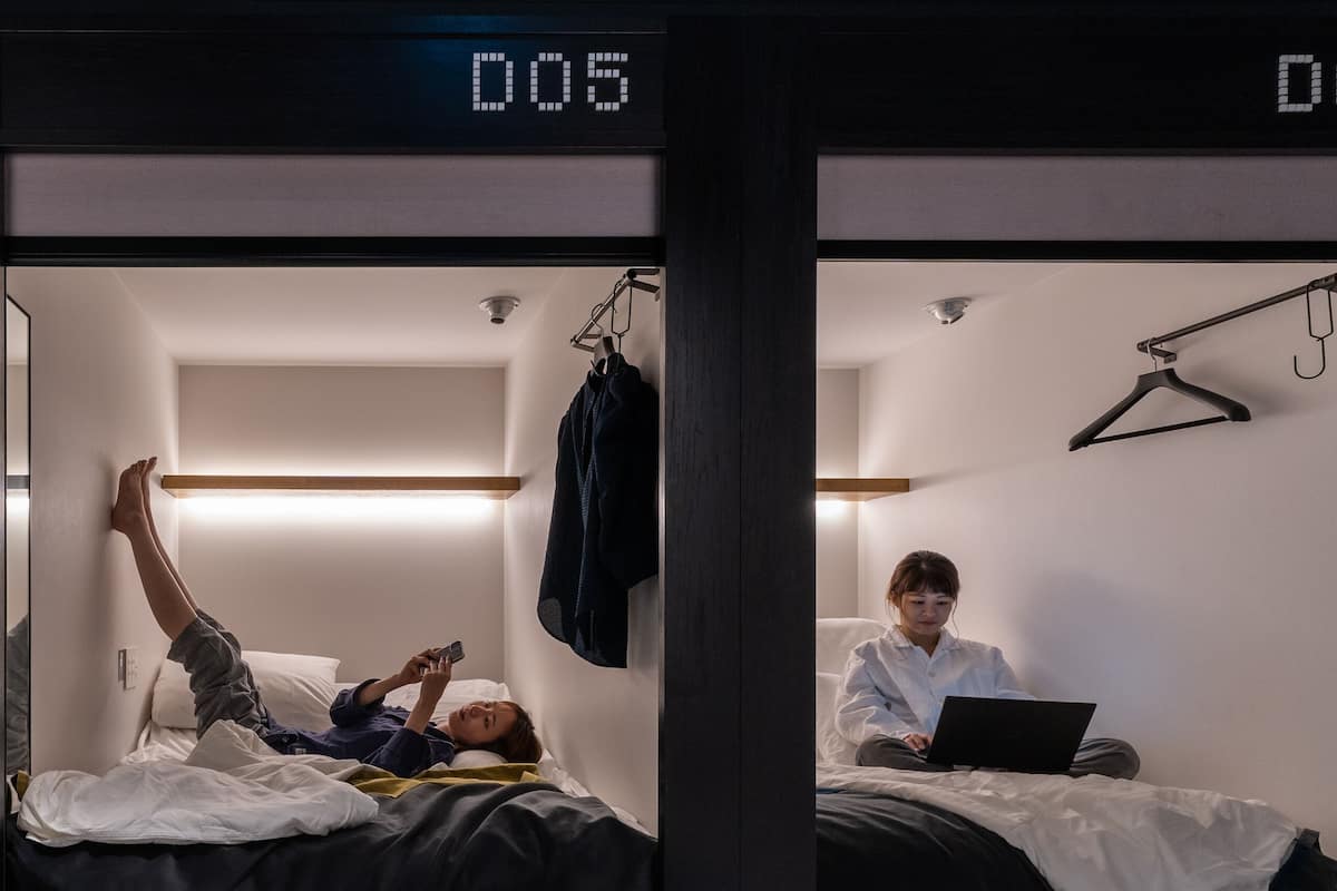 Dois quartos de hotel, um com camas, um com uma pessoa deitada e outro com uma pessoa sentada em um laptop.
