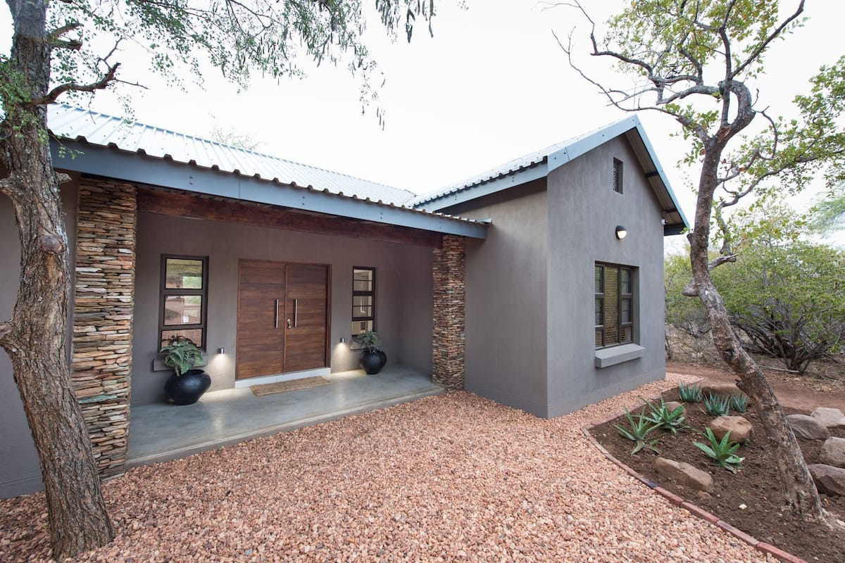 A modern house with a stone facade, large wooden doors, and a gravel driveway.
